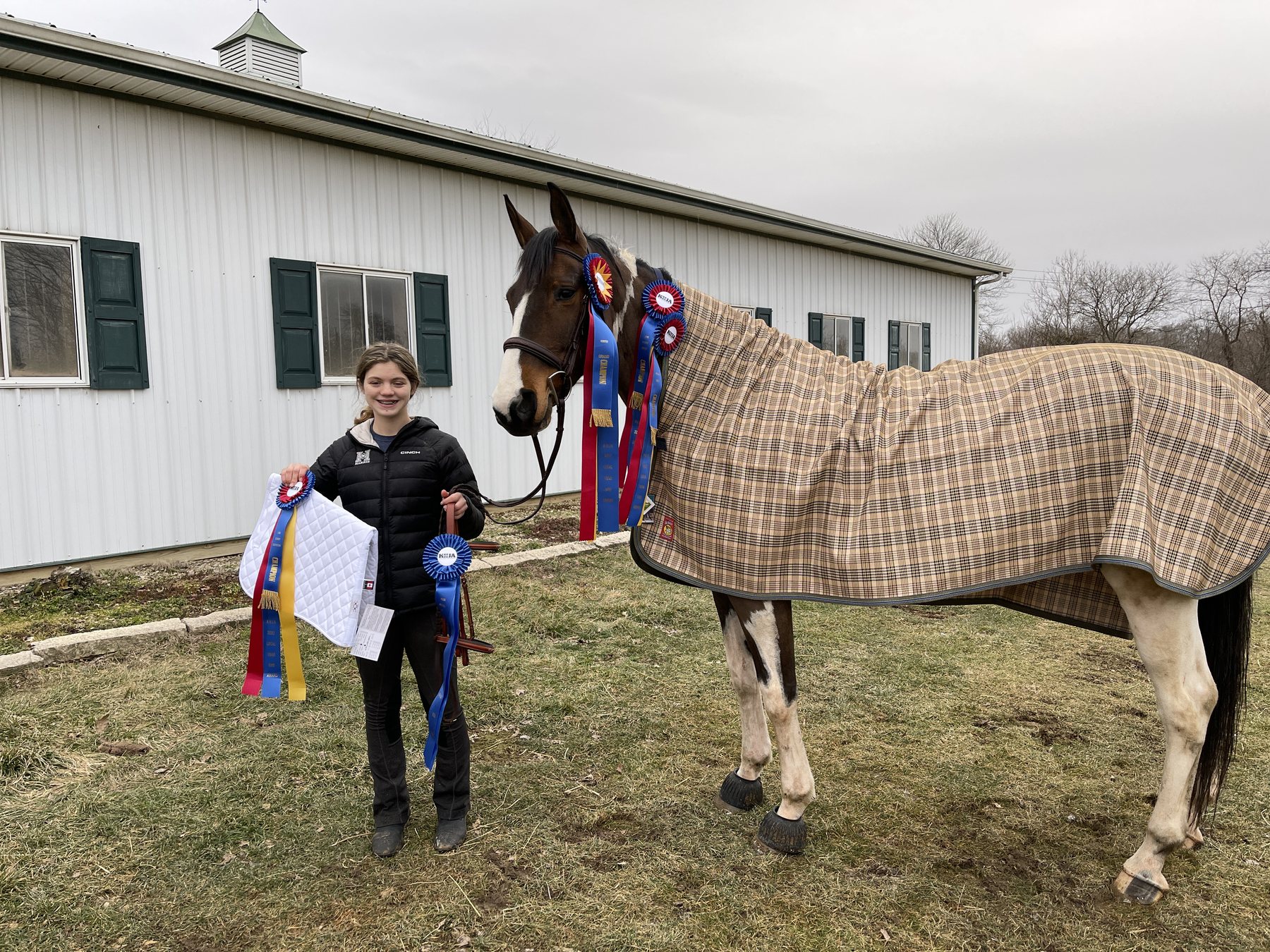 SiSi in her plaid sheet draped with KHJA champion ribbons, Rylee smiling beside her.
