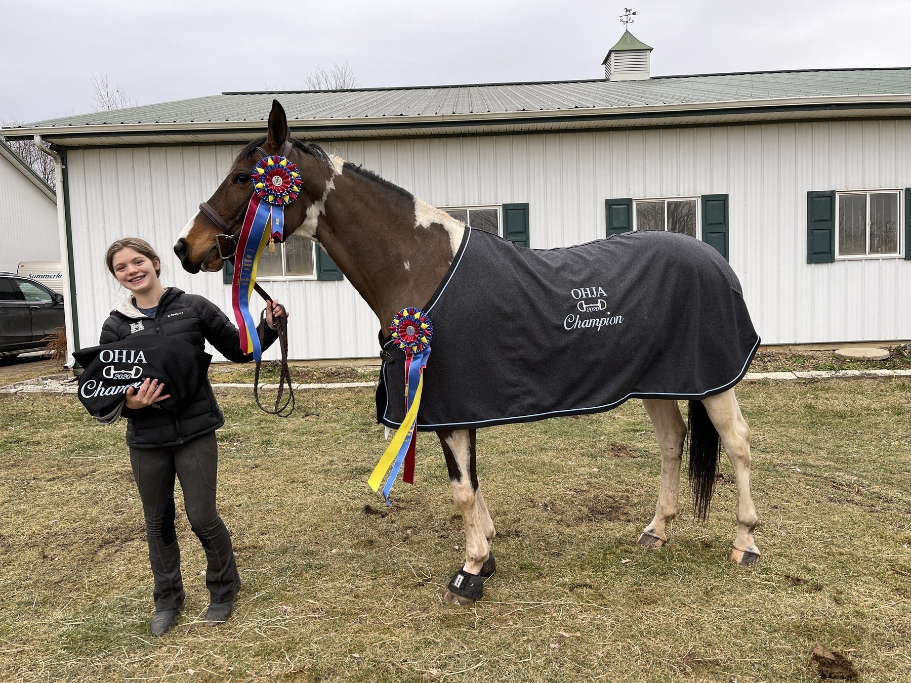 Rylee with a huge smile beside SiSi in her champion cooler and rosettes outside the barn.