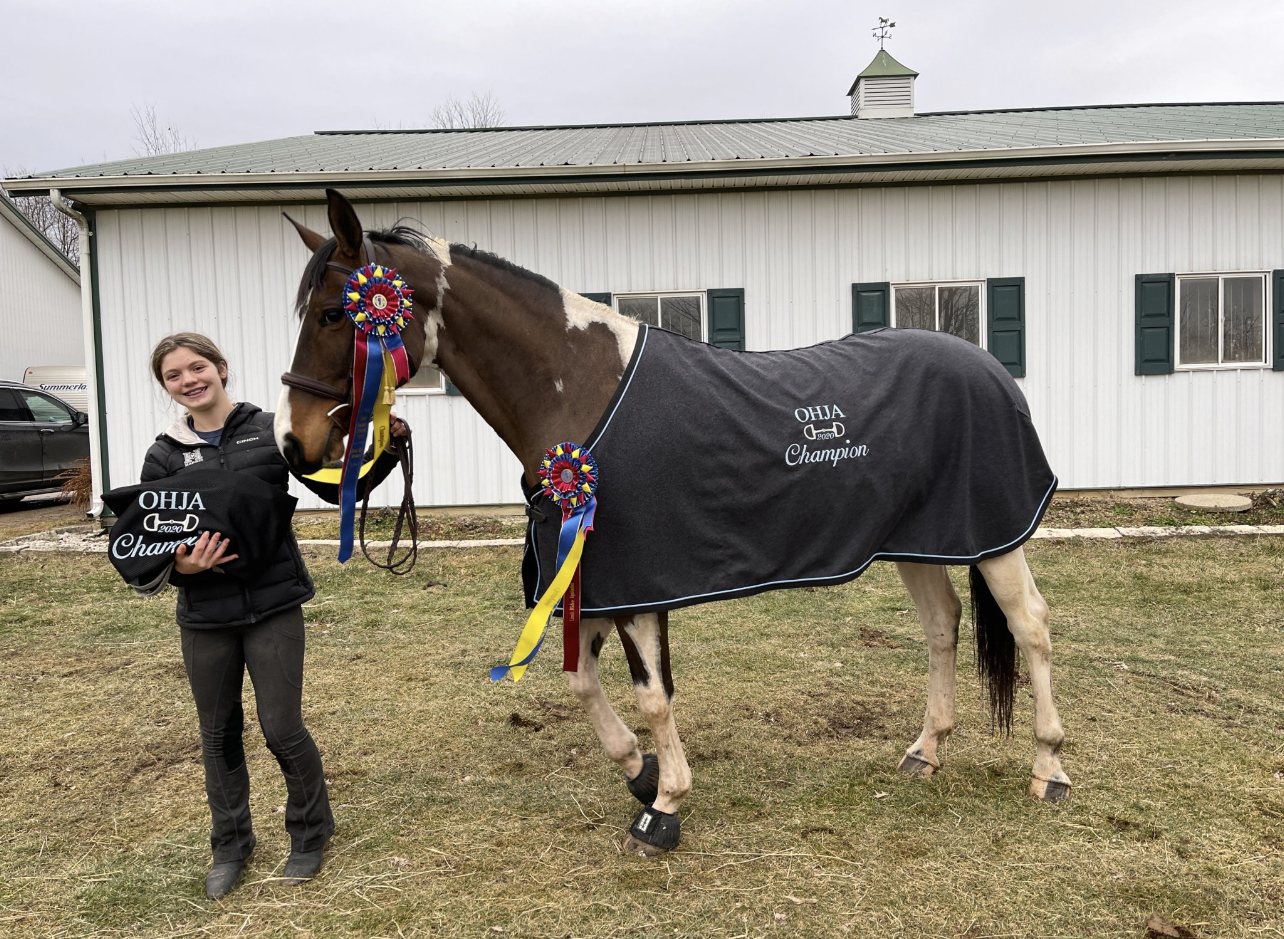 Rylee beside SiSi in her OHJA Champion cooler outside the barn on a March 2021 evening.