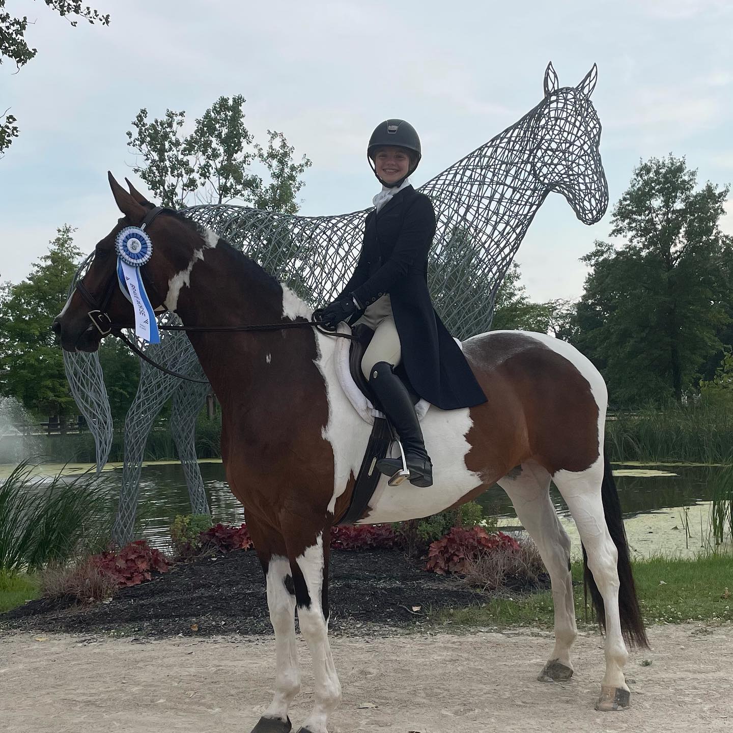 Rylee on SiSi with a Brave Horse ribbon in front of the wire horse sculpture.