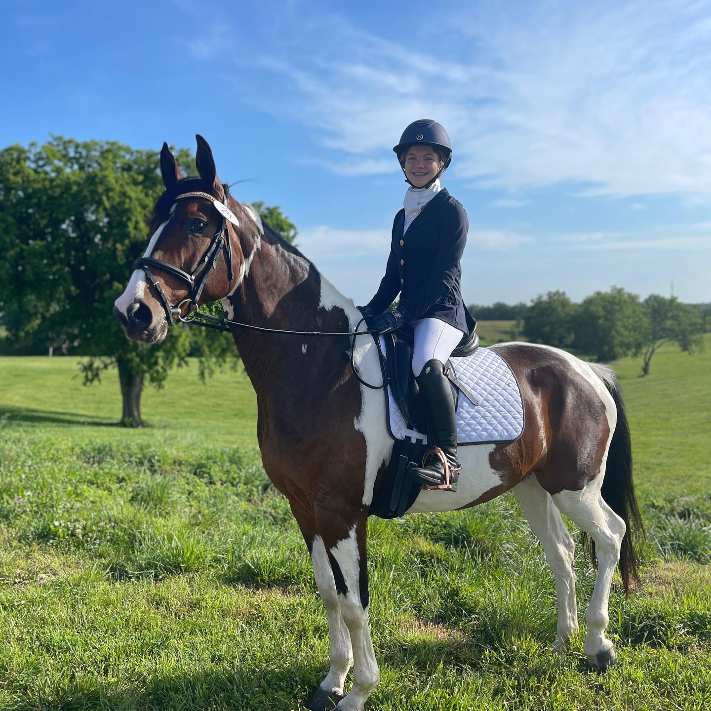 Rylee in dressage attire on SiSi in a green pasture under a blue sky.
