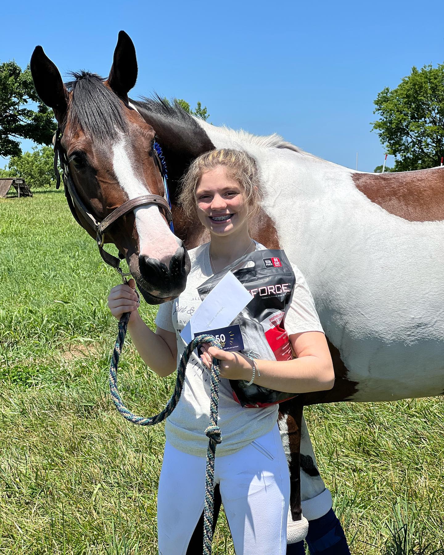 Rylee holding SiSi in a sunny pasture with a prize feed bag and envelope.