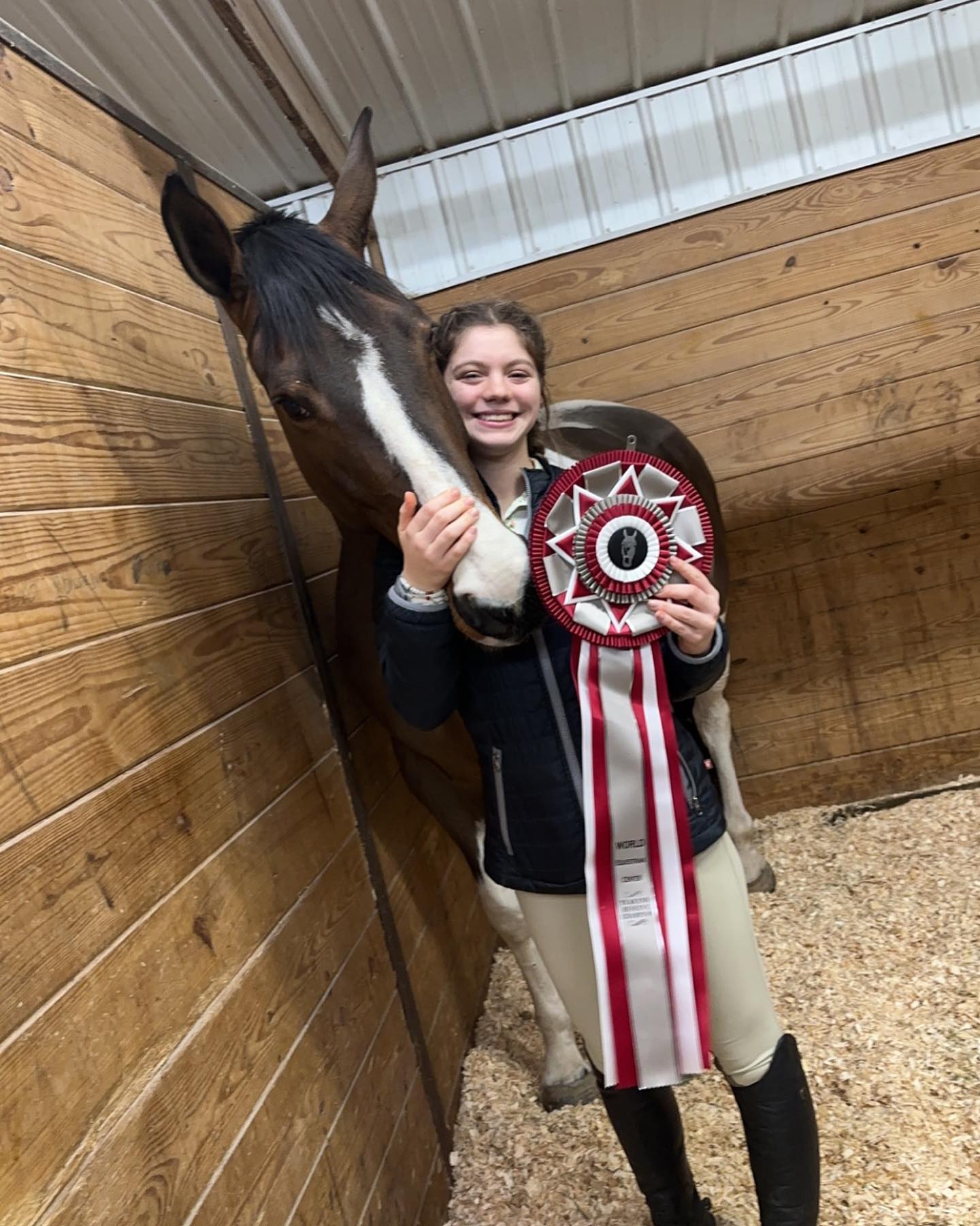 Rylee hugging SiSi in her stall while holding a large red-and-white rosette.