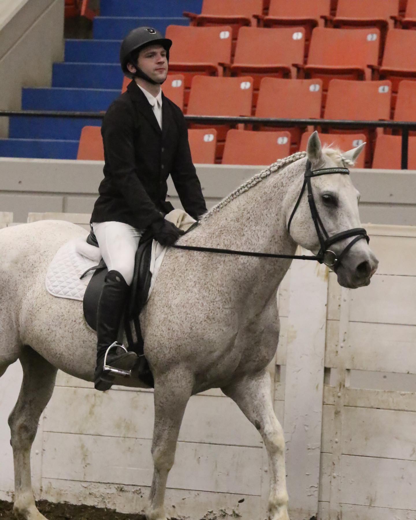 Kaleb in hunt-seat attire riding Snowflake, mane braided, at the coliseum.