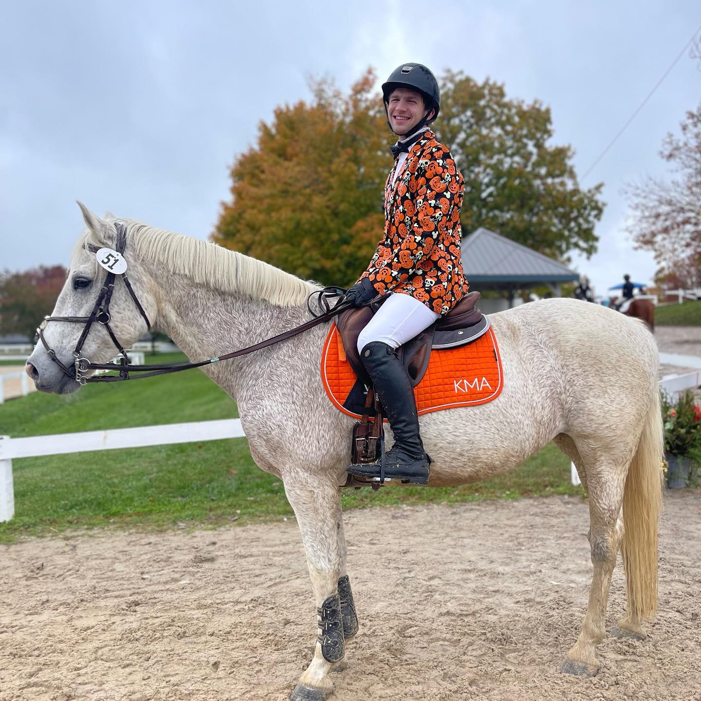 Kaleb in a Halloween pumpkin show coat riding Snowflake.