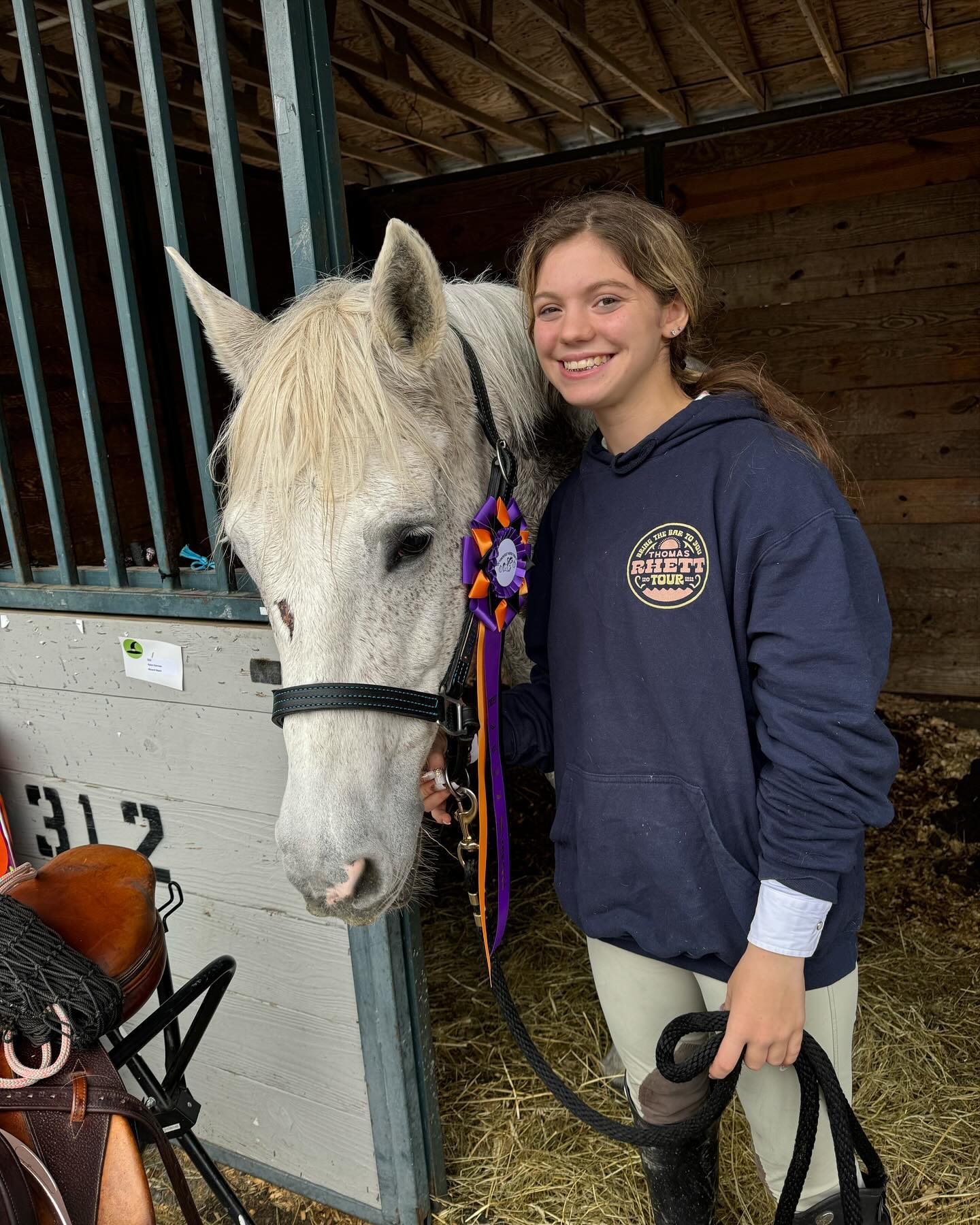 Rylee smiling with Snowflake and a purple-and-orange rosette at stall 312.