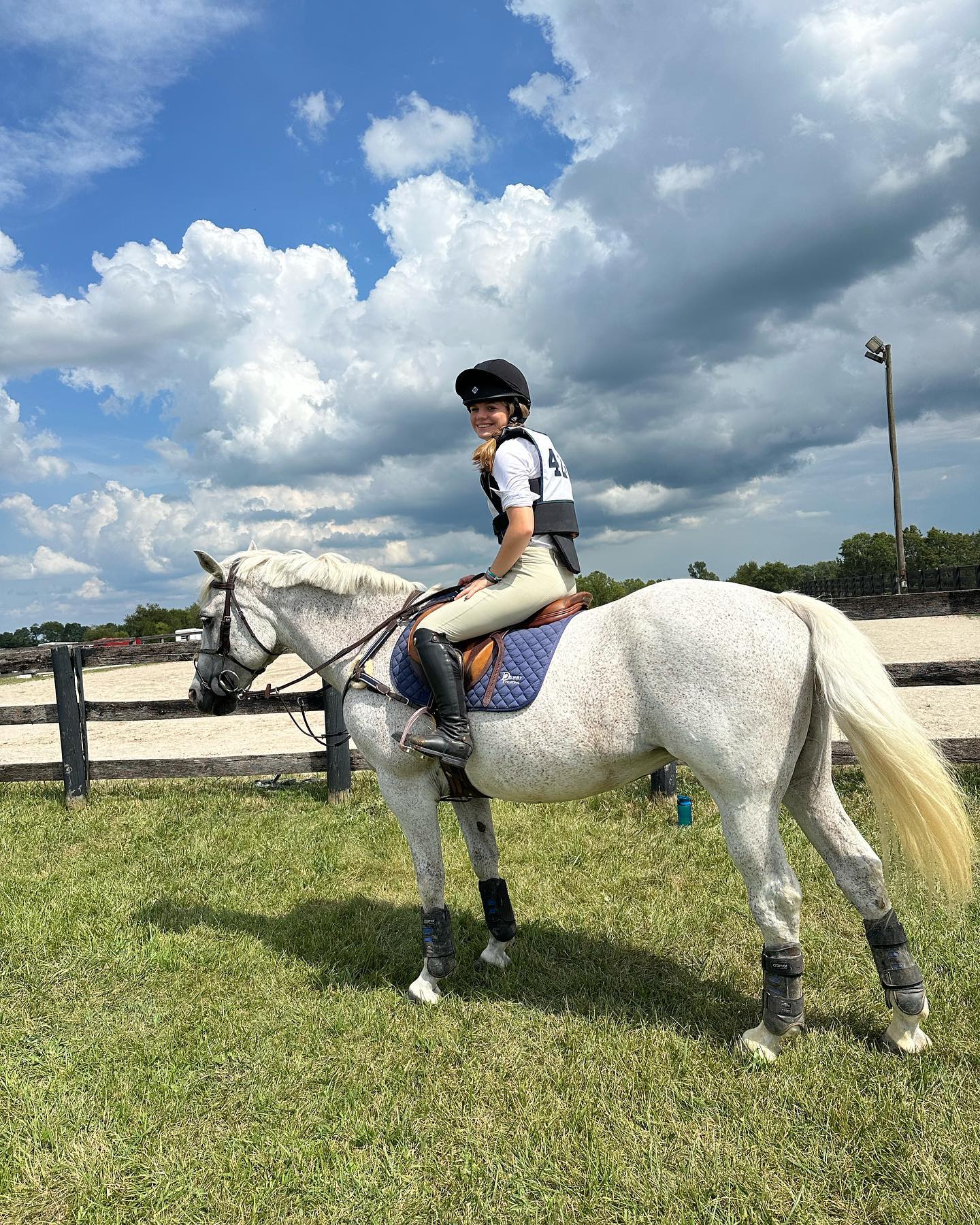 Rylee mounted on Snowflake in cross-country gear under a dramatic sky.