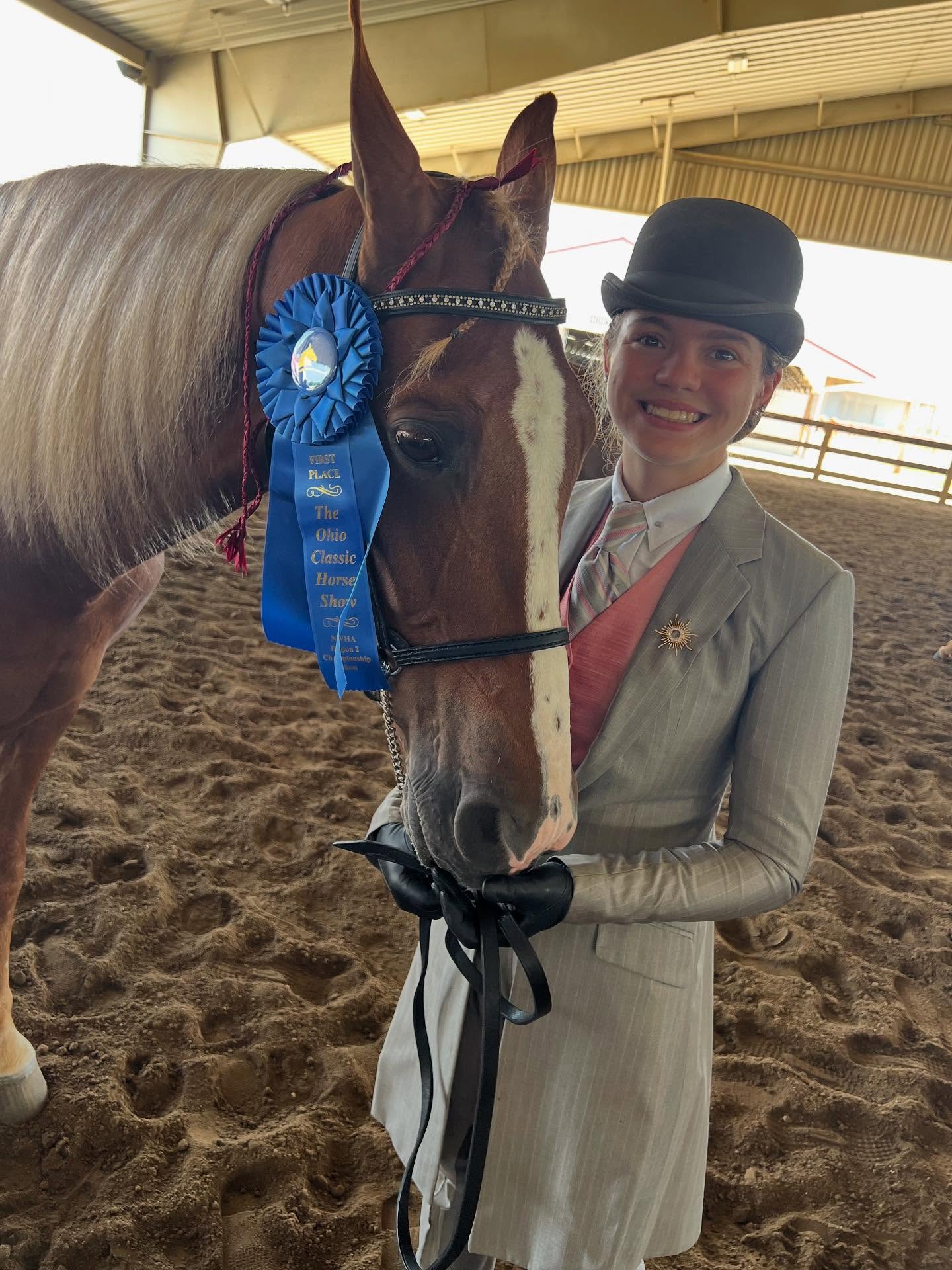 Rylee with a big smile holding an Ohio Classic first-place ribbon beside Sonny's flaxen-maned blaze face.