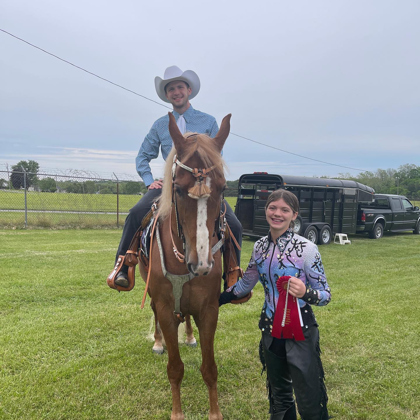 Kaleb mounted western on Sonny while Rylee stands alongside in a sparkle show shirt with a red ribbon.