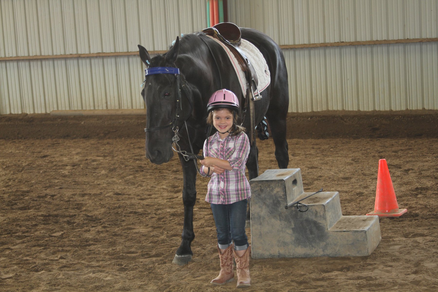 Six-year-old Rylee in her pink helmet holding the lead and grinning beside the black horse.