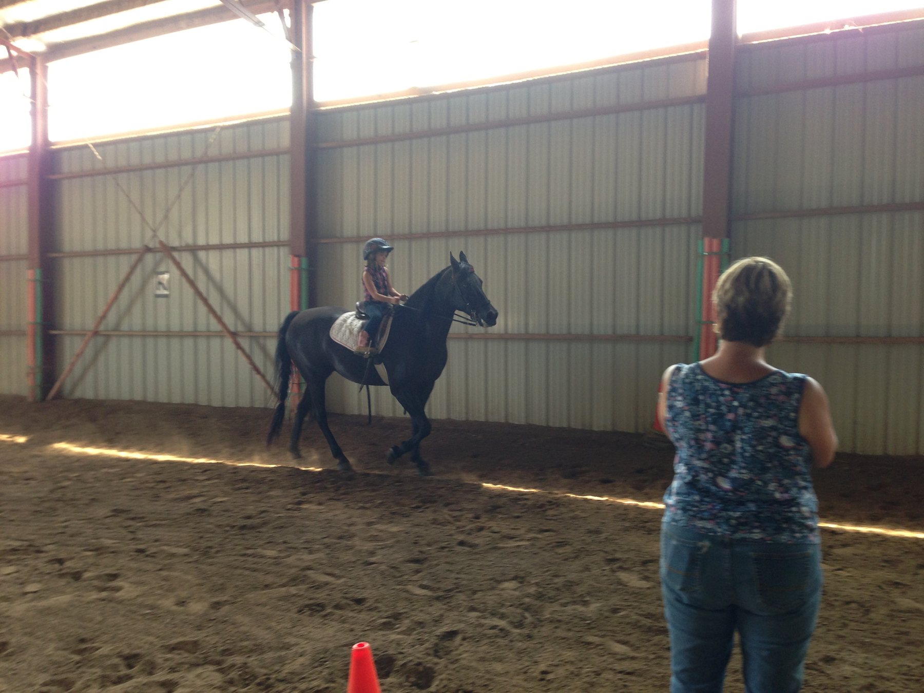 Rylee sitting upright on the black horse in the arena in good evening light.