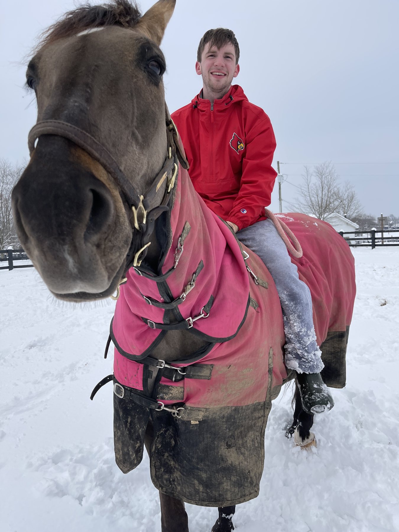 A curious horse nose pokes into the frame as Kaleb plays beside the blanketed buckskin.