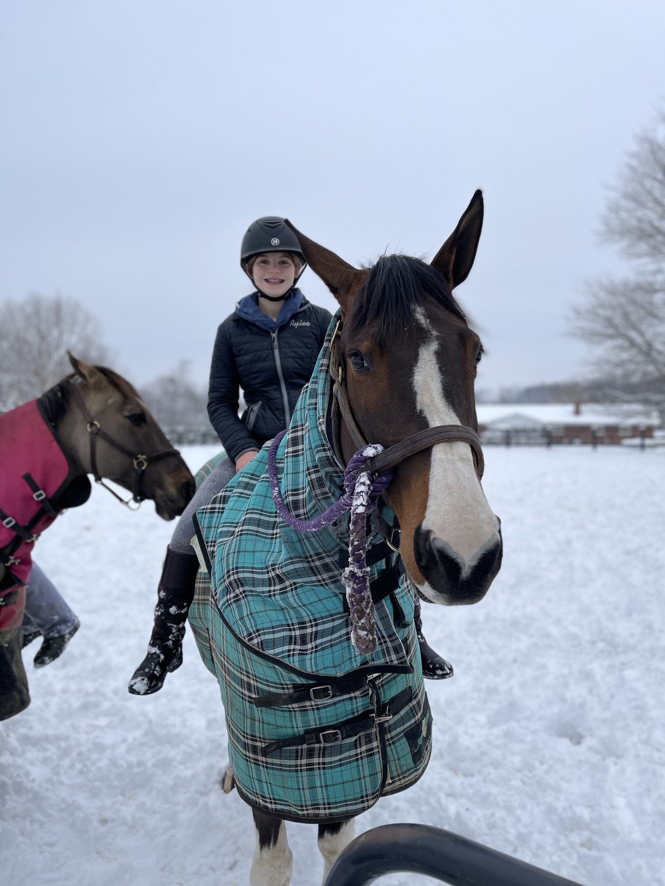 Rylee in her helmet astride a bay pinto in a teal plaid blanket, deep snow all around.