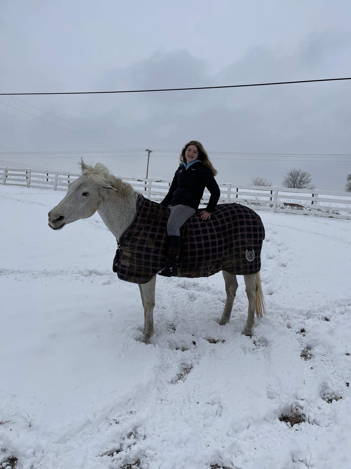 Rylee smiling as she rides the blanketed gray bareback through deep snow.