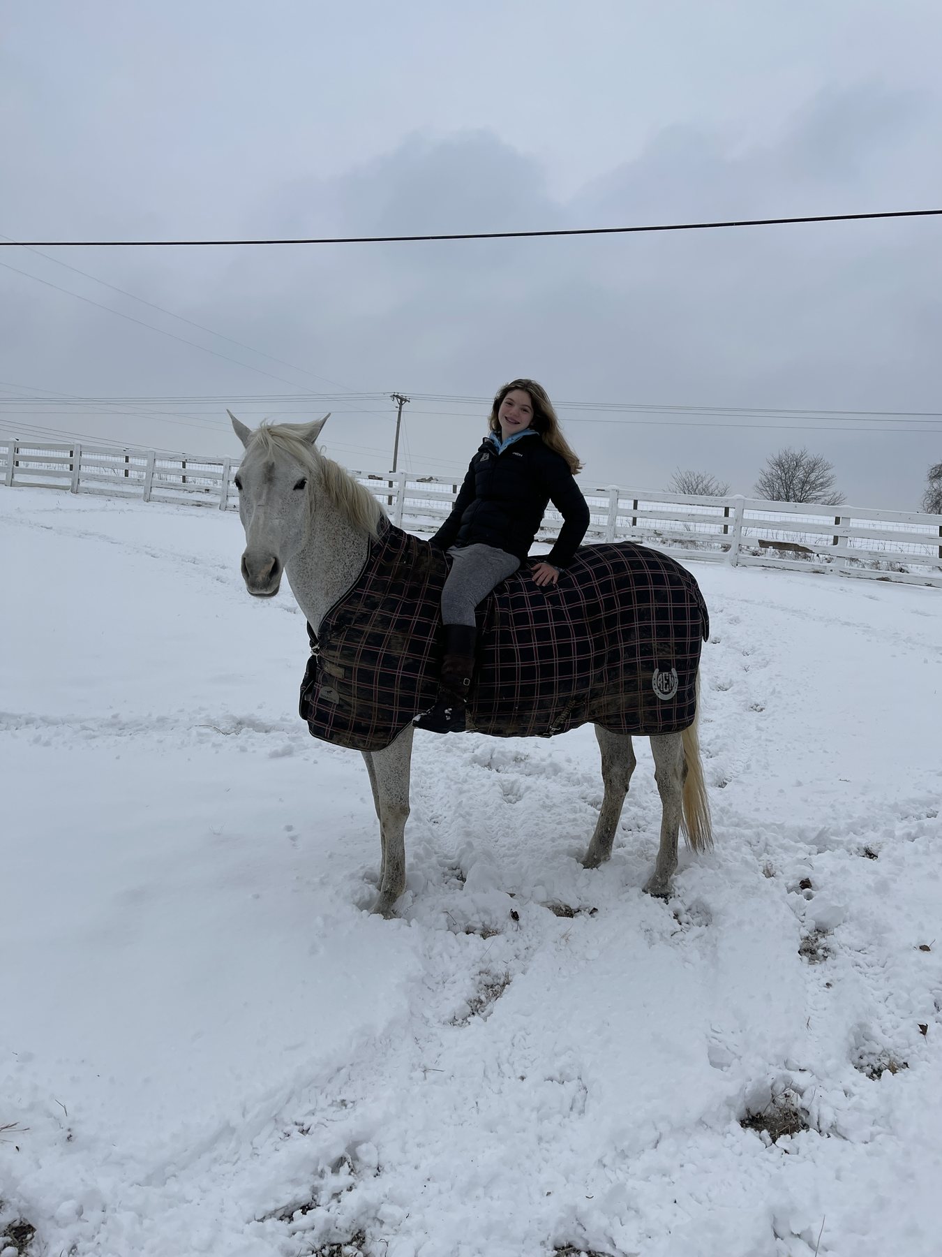 Rylee riding the plaid-blanketed gray through the snowy paddock.