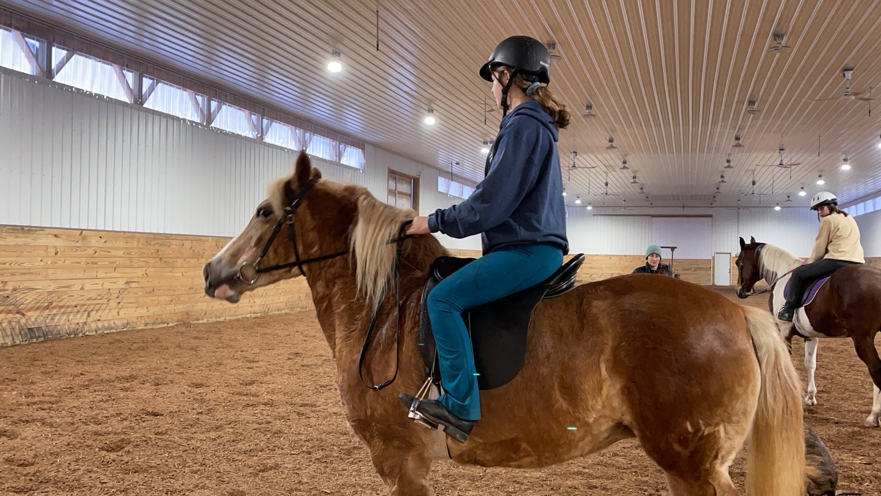 Rylee riding a flaxen palomino lesson horse under the indoor arena lights.