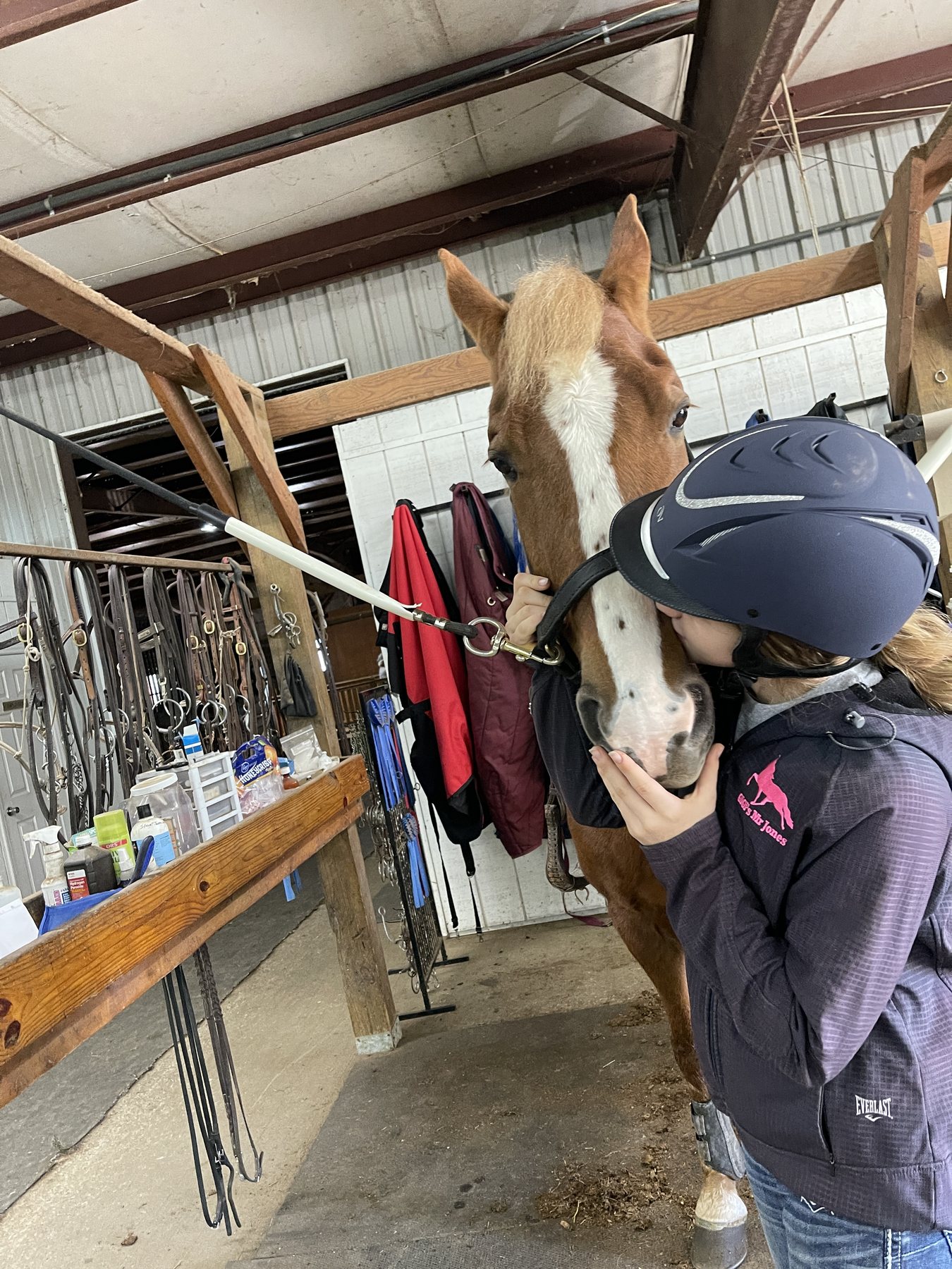 Rylee in her helmet kissing the flaxen chestnut pony's muzzle in the barn aisle.