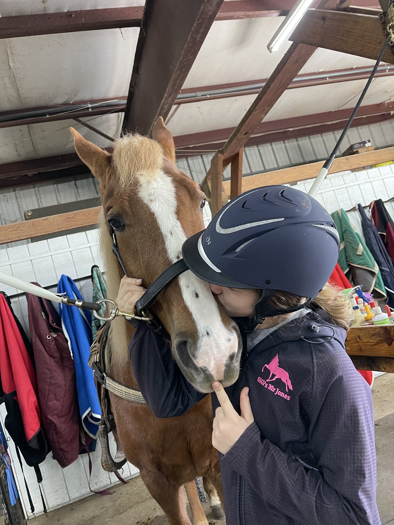 Rylee planting a kiss on the chestnut's nose in the barn aisle.