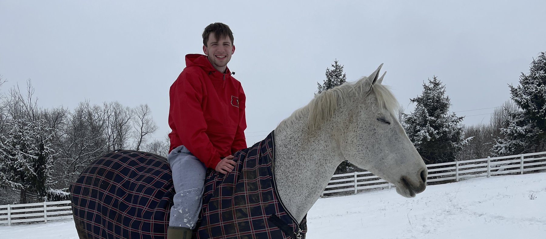 Kaleb Alden smiling astride a blanketed gray horse in a snowy paddock.