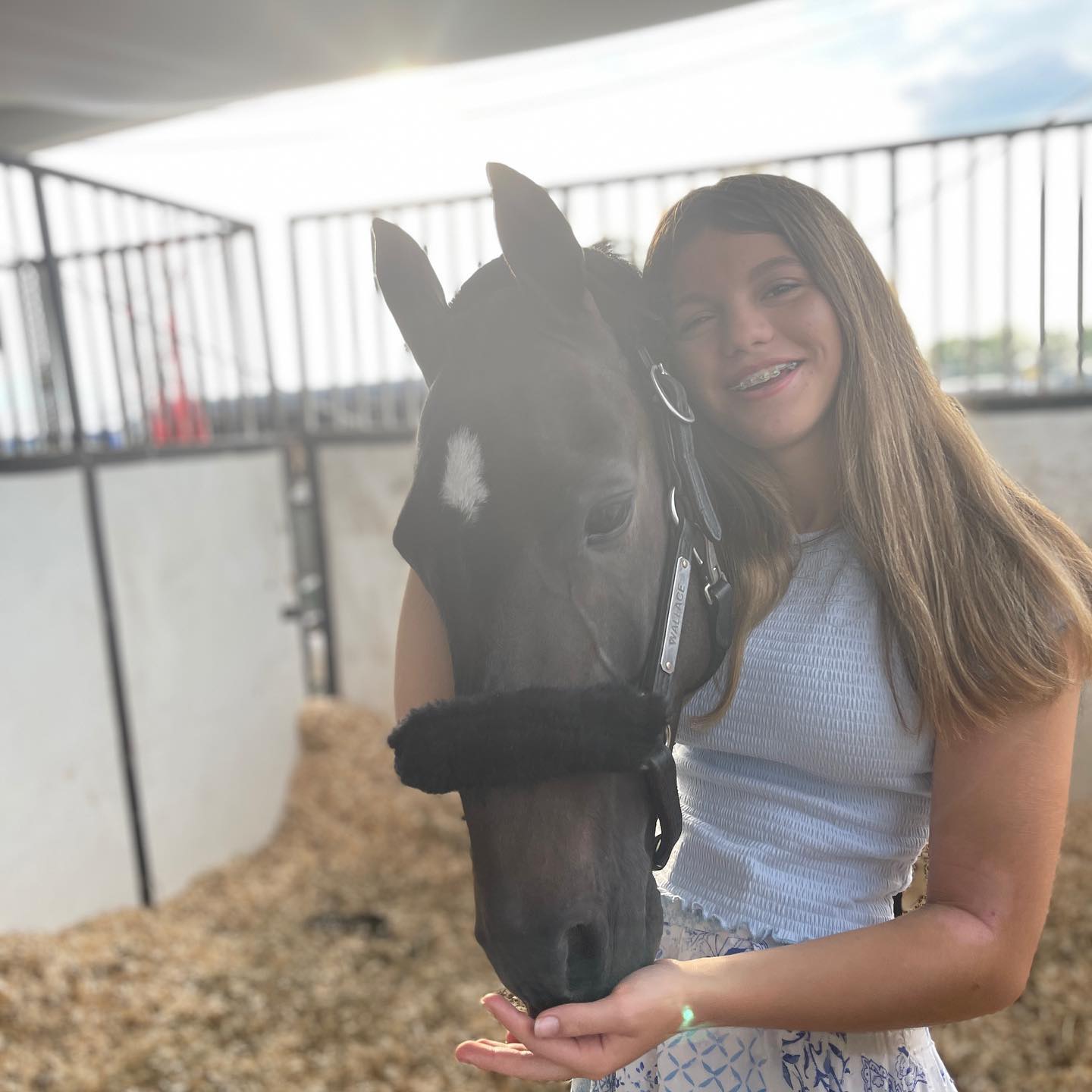 Rylee hugging a dark horse in a backlit stall.