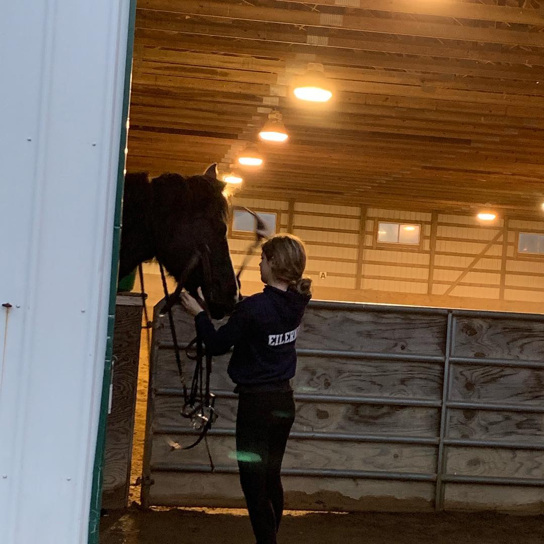 Rylee in an EILERMAN hoodie bridling a black horse at Briarwood Farm.