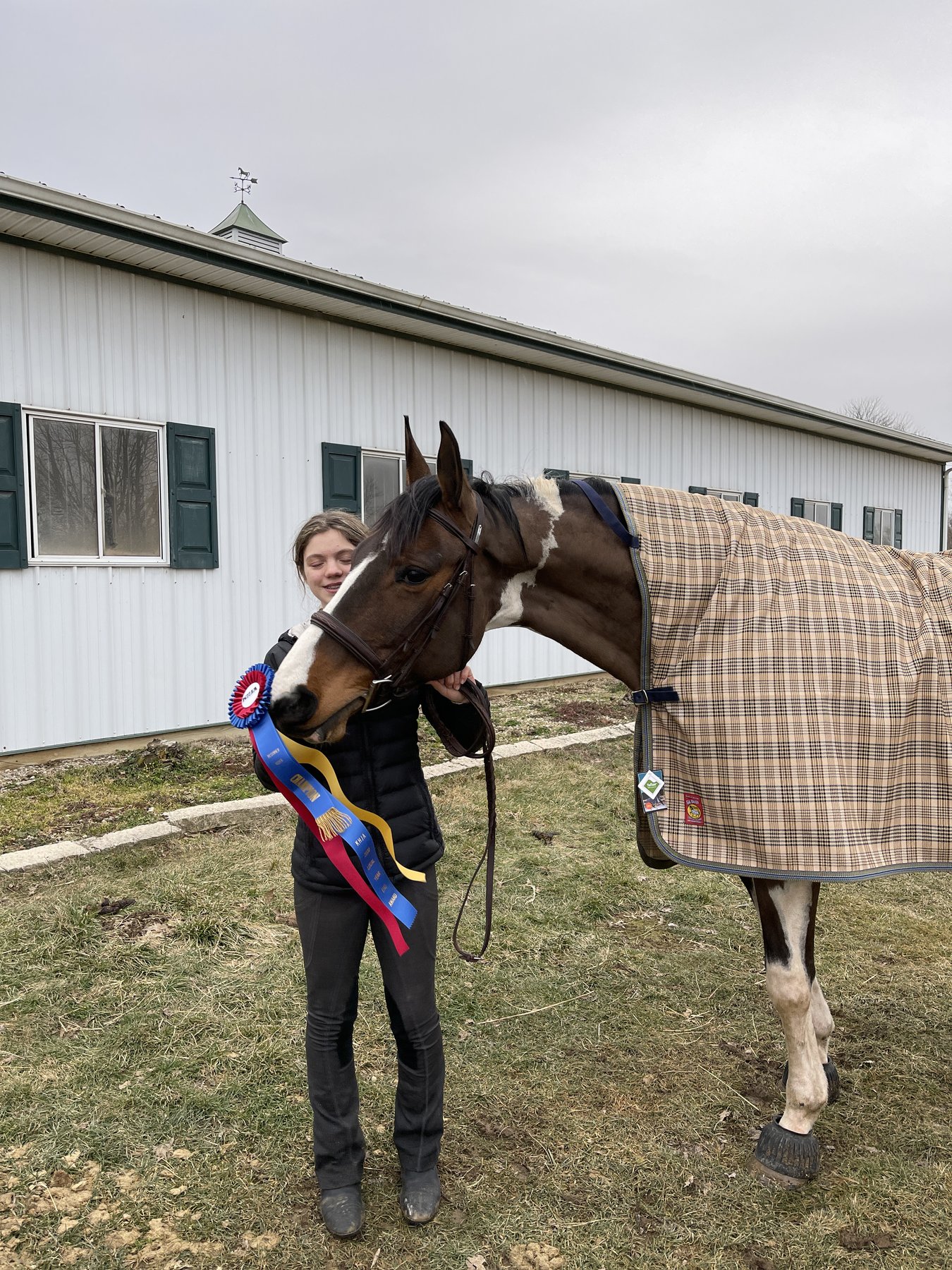 Rylee with SiSi, her bay-and-white pinto mare, wearing a champion ribbon outside the barn in 2021.