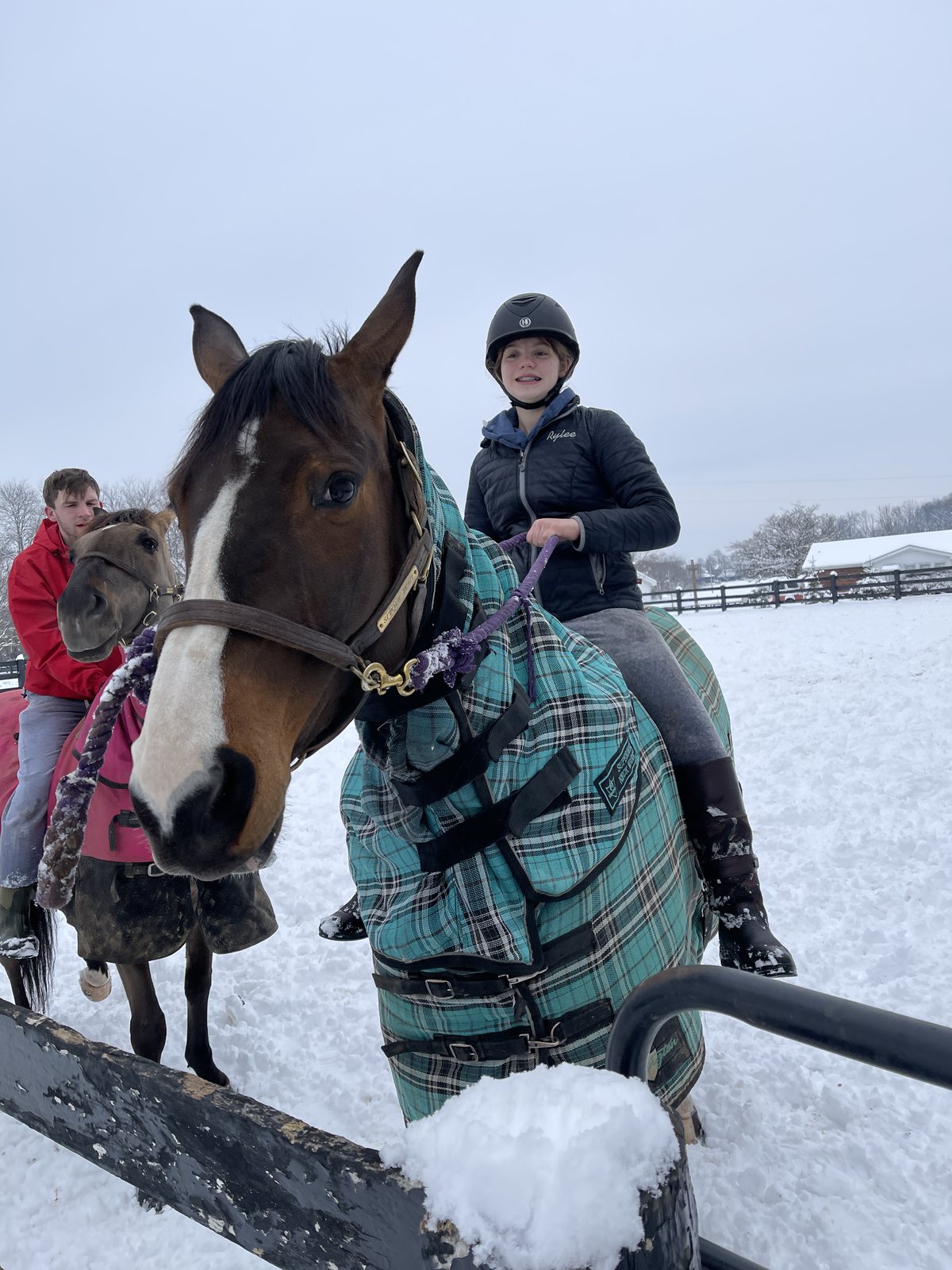 Rylee astride a blanketed horse in the snow, with Kaleb on a pony behind her.