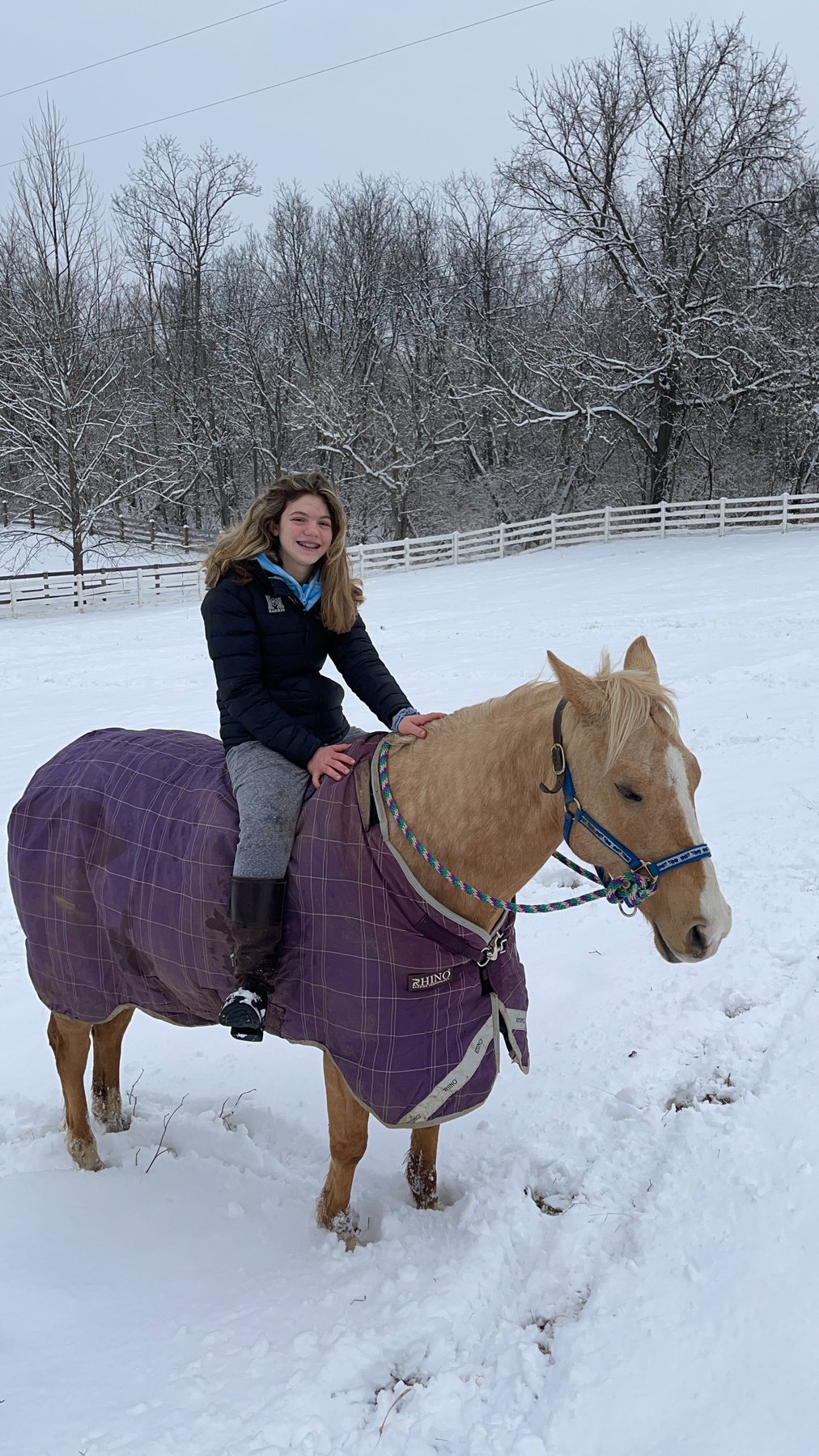 Rylee riding a blanketed palomino bareback through fresh snow.