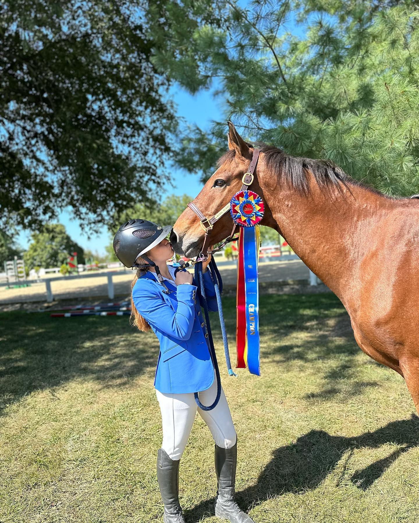 Rylee in a blue coat kissing a bay horse wearing the Fall Classic champion neck ribbon.