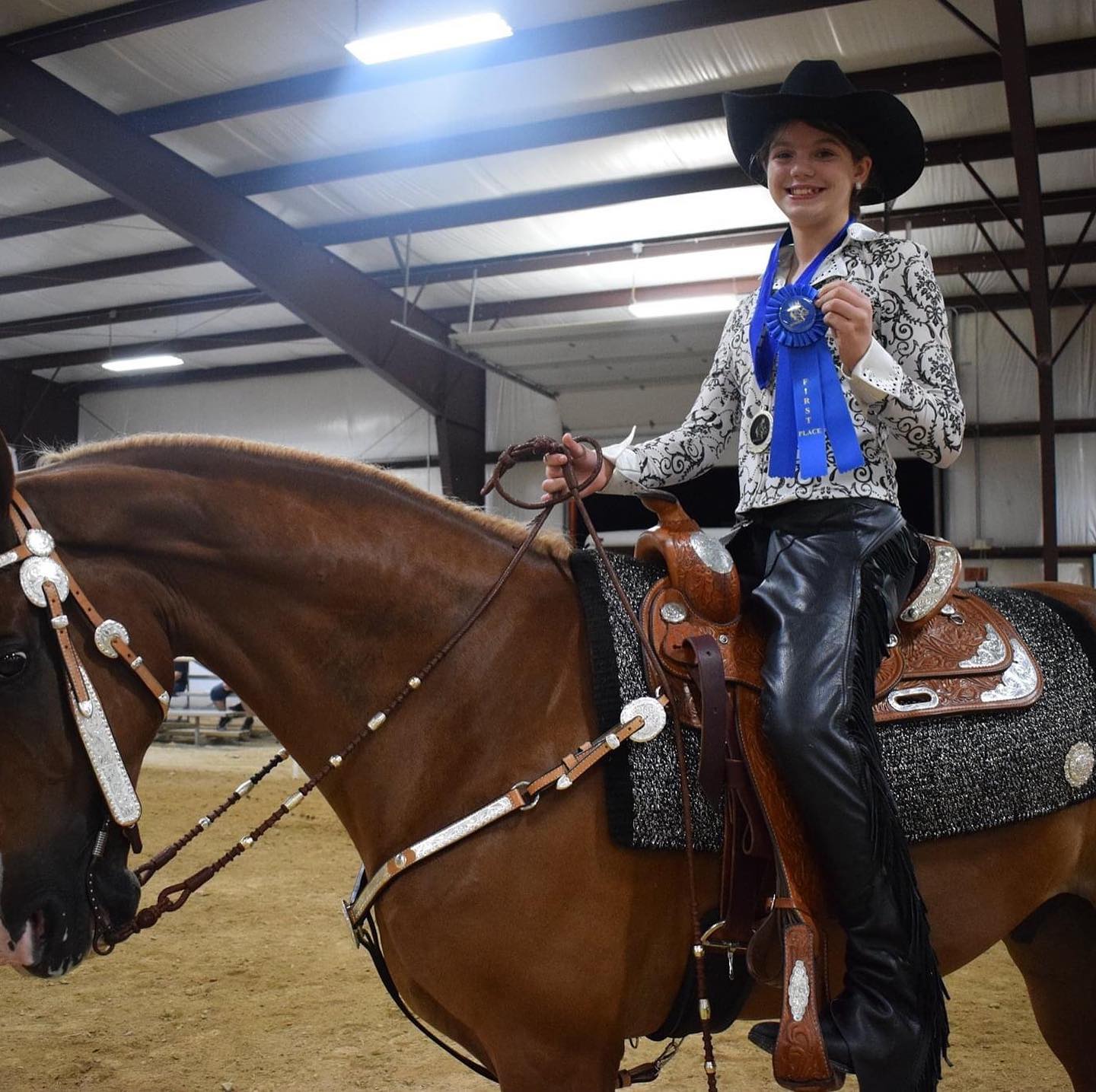 Rylee in western show attire with a first-place rosette beside a horse in silver show tack.