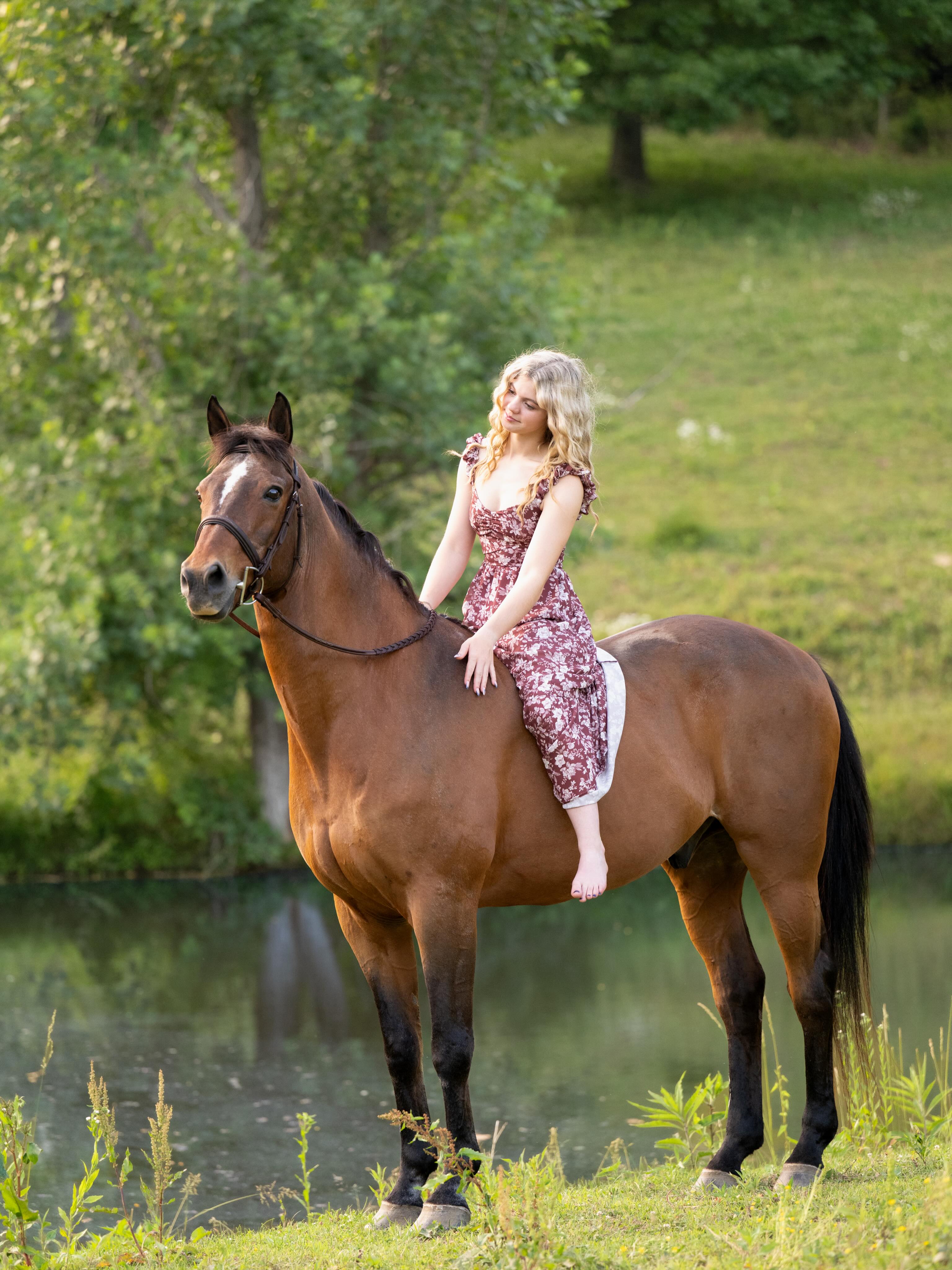 Golden-hour photoshoot of Rylee with a bay horse in a bareback pad by the pond.