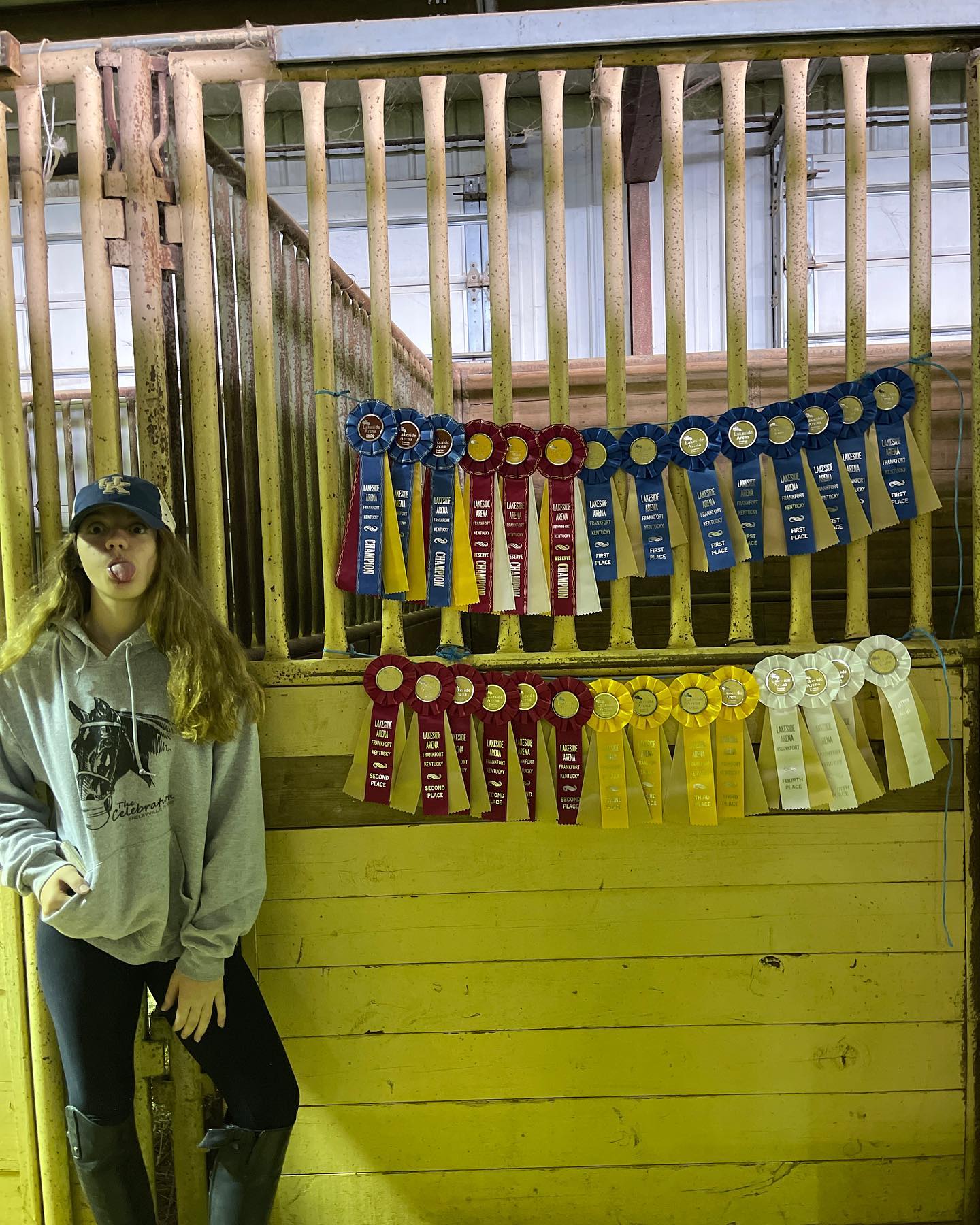 Rylee in a UK cap, tongue out, beside the big ribbon wall at Lakeside Arena.