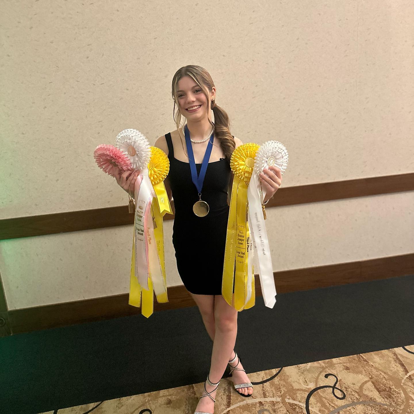 Rylee in a black dress holding Ohio hunter-jumper year-end rosettes and a medal.