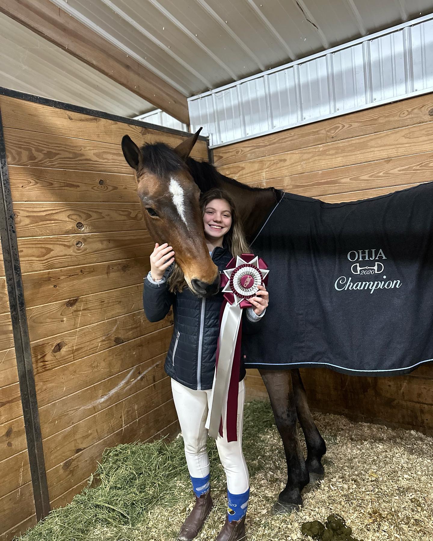 Rylee with a bay in the OHJA 2020 Champion cooler and a rosette in the stall.