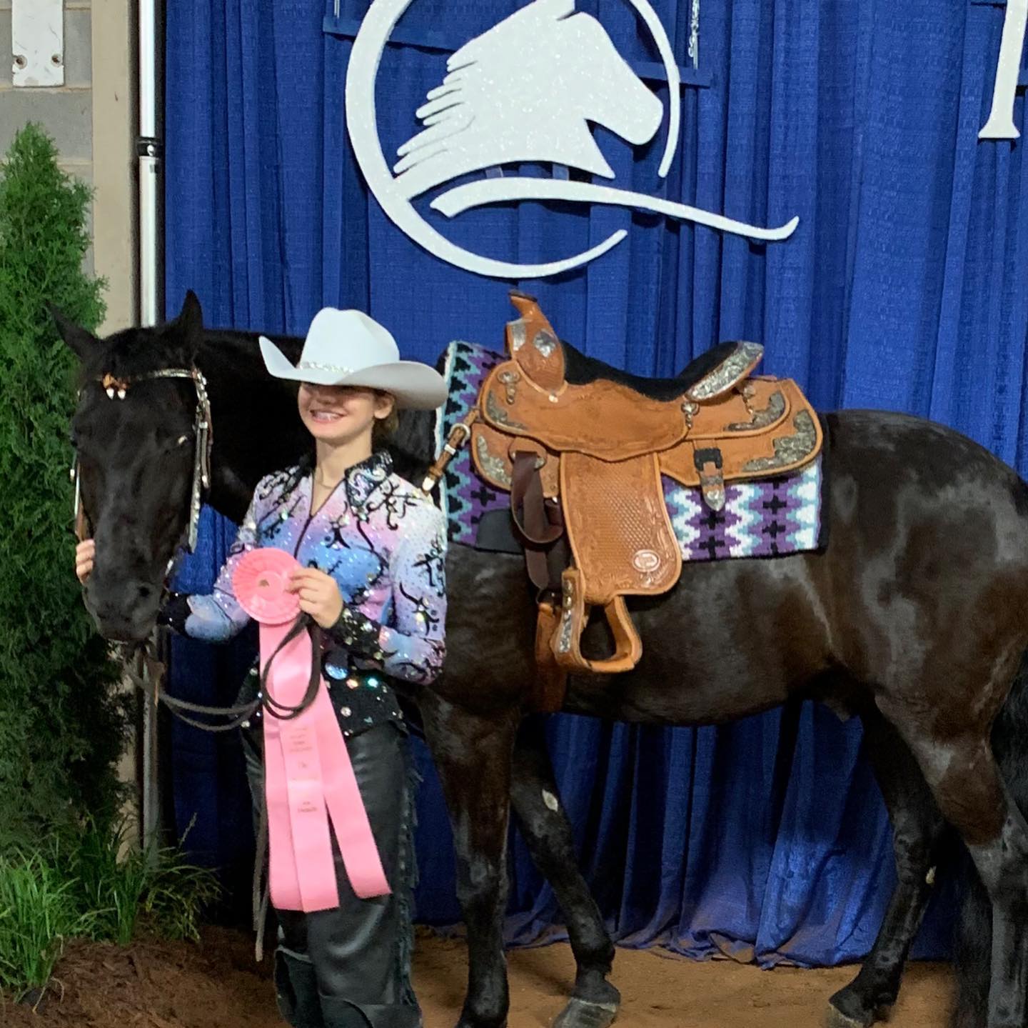Rylee in a white hat with a black horse and pink ribbon at the show backdrop.