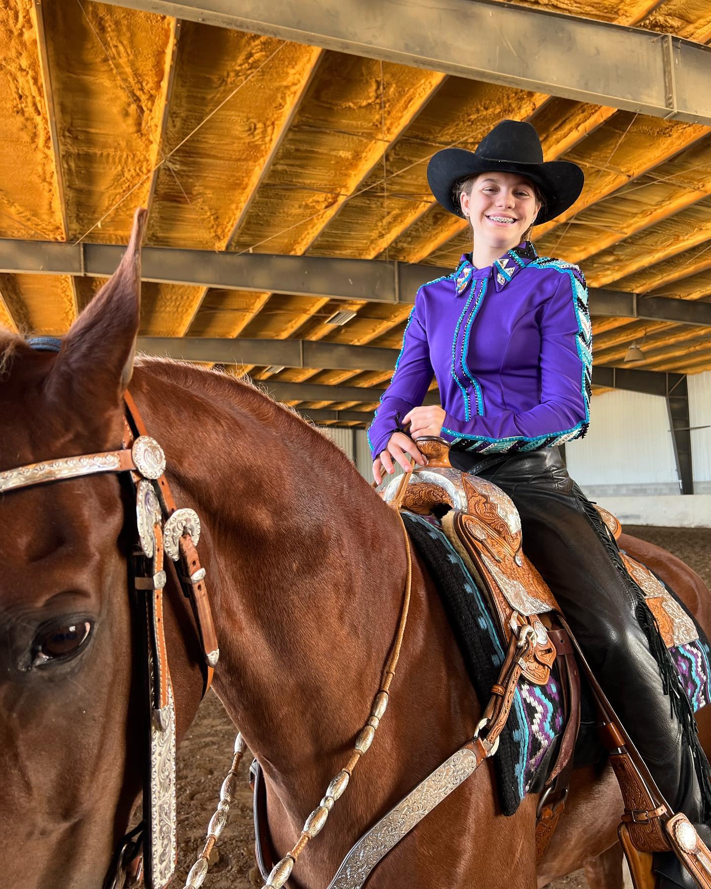 Rylee in a purple western show outfit and black hat mounted on a sorrel.