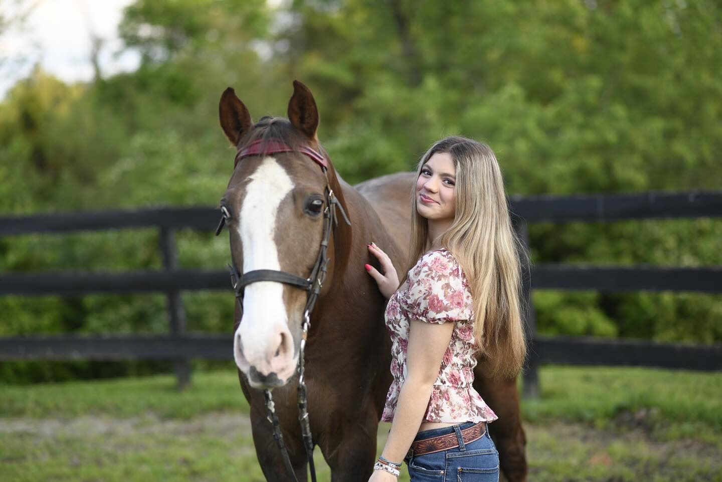 Golden-hour pasture portrait of Rylee with a wide-blazed horse in a red halter.
