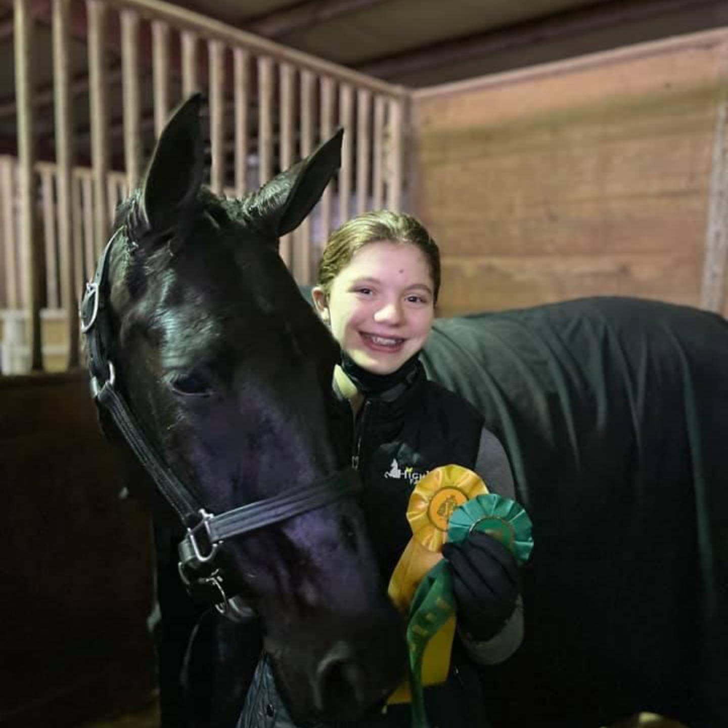 Rylee with a black horse and yellow and green ribbons in the stall.