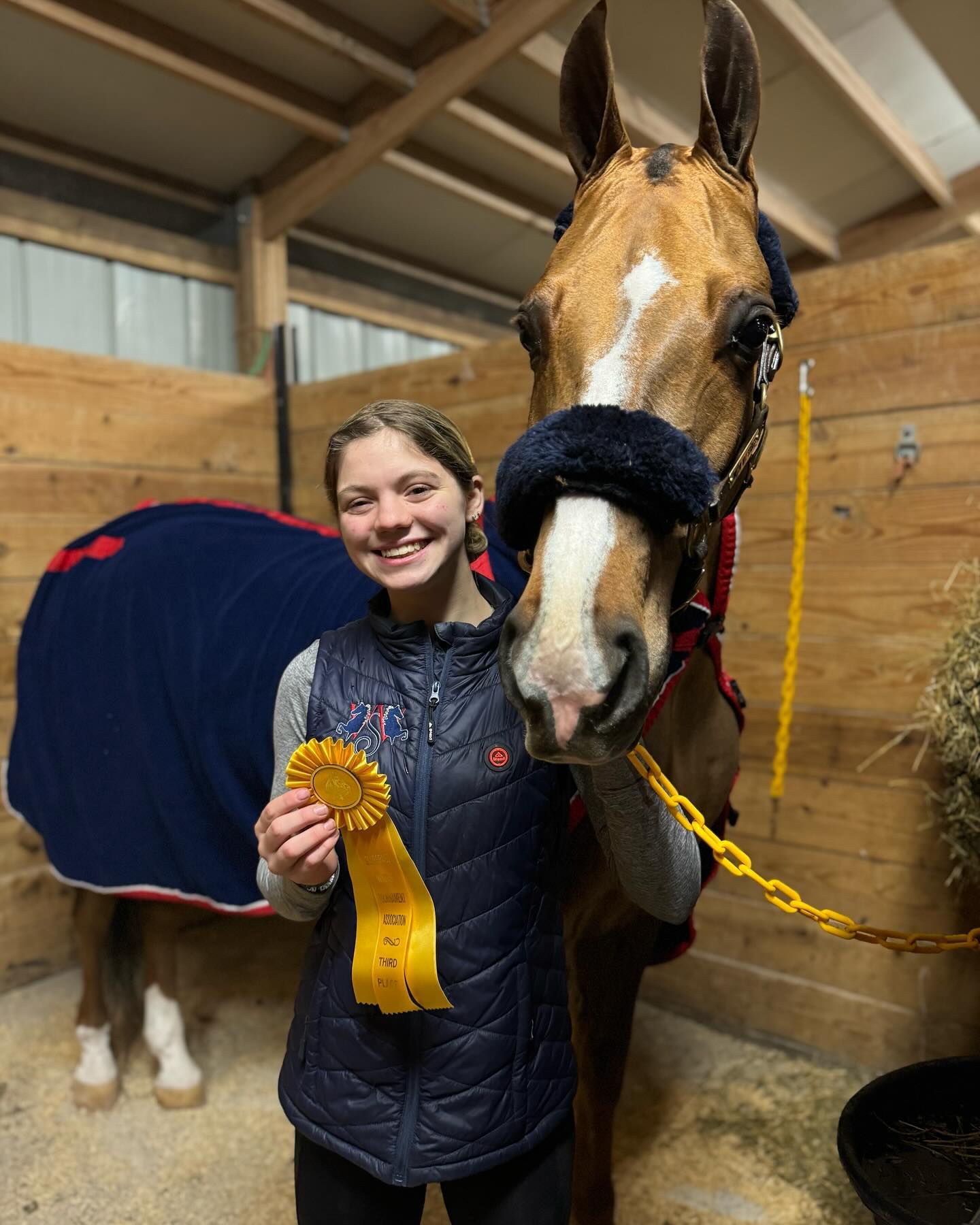 Rylee with a third-place ribbon beside a blanketed horse in the stall.