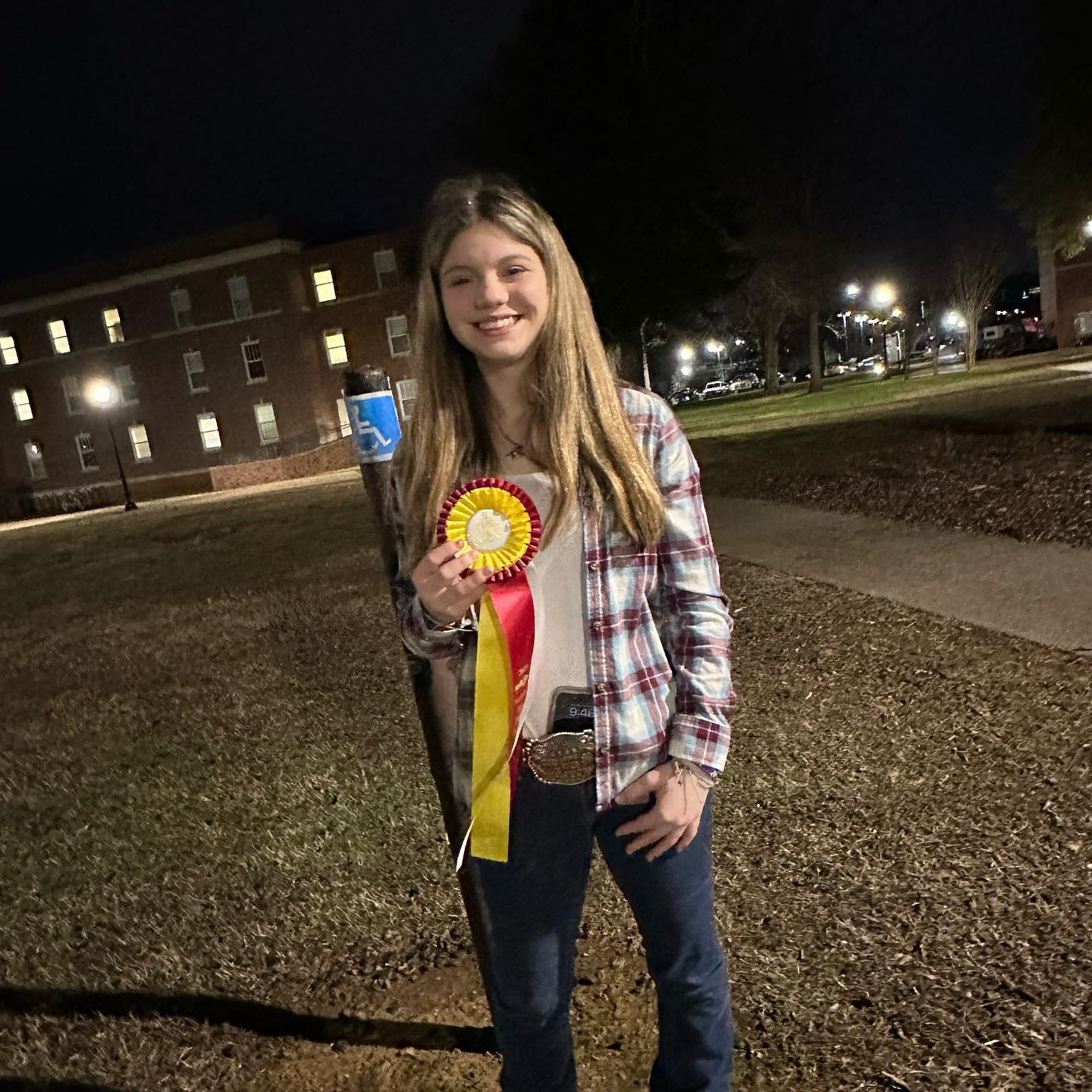 Rylee at night with a red-and-yellow rosette and a trophy belt buckle.
